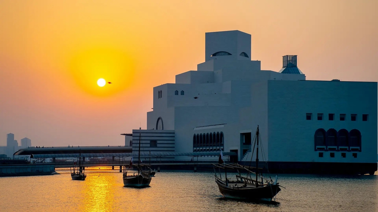 The geometric Museum of Islamic Art building at sunset with dhow boats in the water.