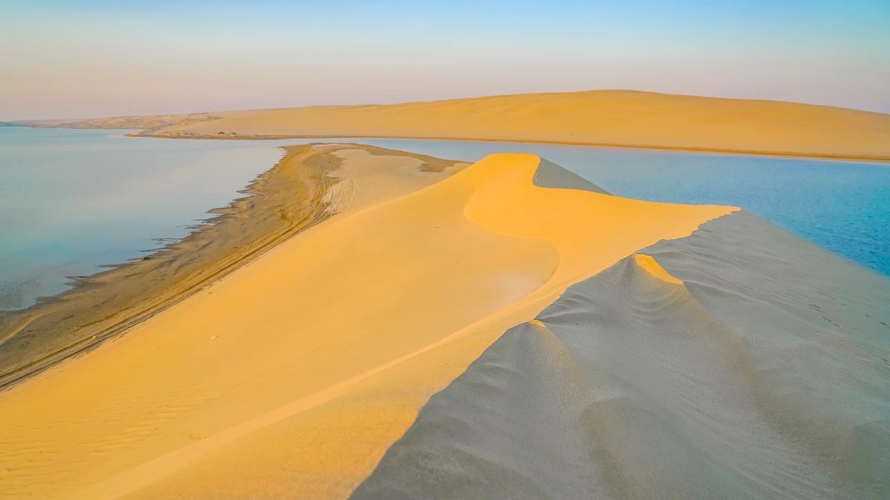 Two white Toyota Land Cruisers dune bashing across golden sand dunes during sunset on a desert safari in Doha, Qatar