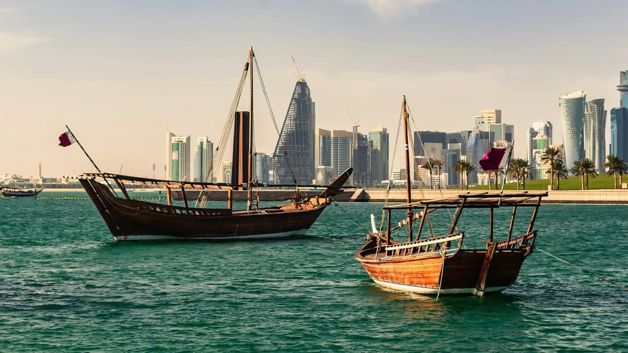 Traditional wooden dhow boats floating on calm water along the Doha Corniche skyline.