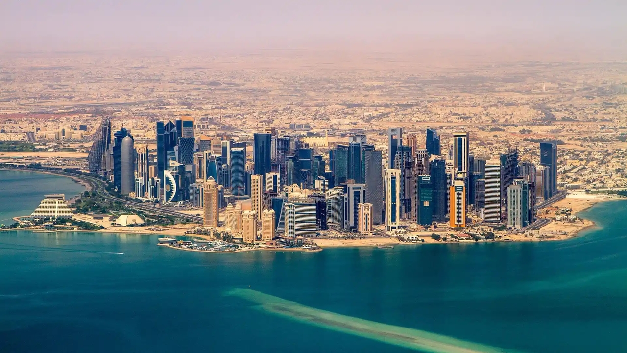 High-angle aerial view of Doha’s West Bay skyscrapers along the blue coastline.