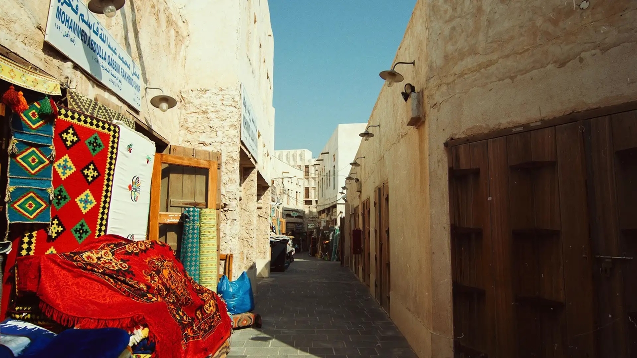 A narrow alleyway in Souq Waqif lined with traditional stone walls and vibrant, patterned carpets on display.