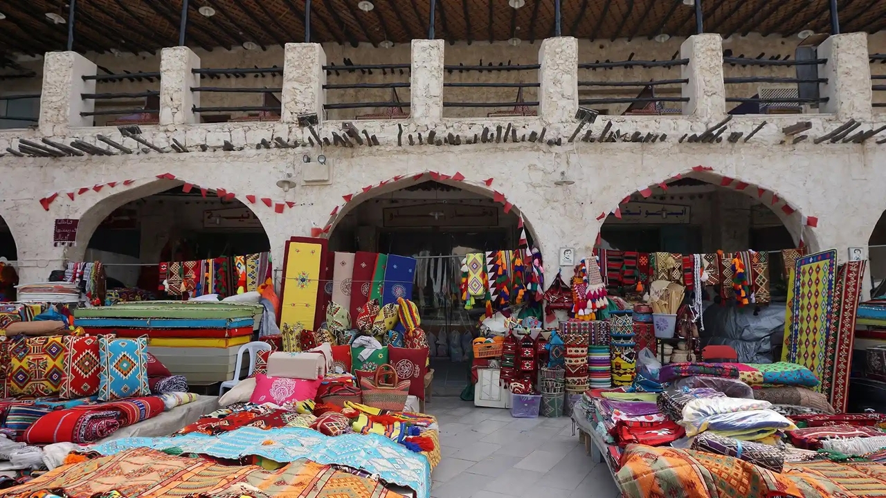 Colorful woven textiles, rugs, and pillows on display at a Souq Waqif market stall.