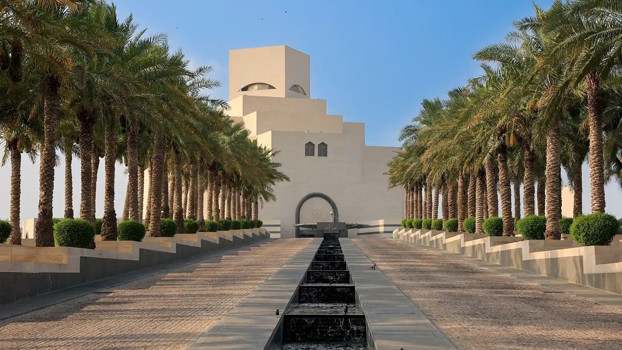 The geometric architecture of the Museum of Islamic Art in Doha, lined with palm trees.