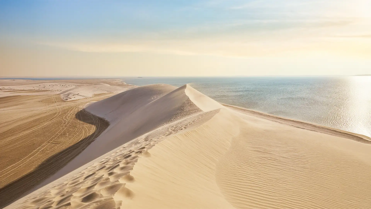 Aerial view of white sand dunes meeting the calm blue waters of the Arabian Gulf at Khor Al Adaid during a desert safari from Doha, Qatar