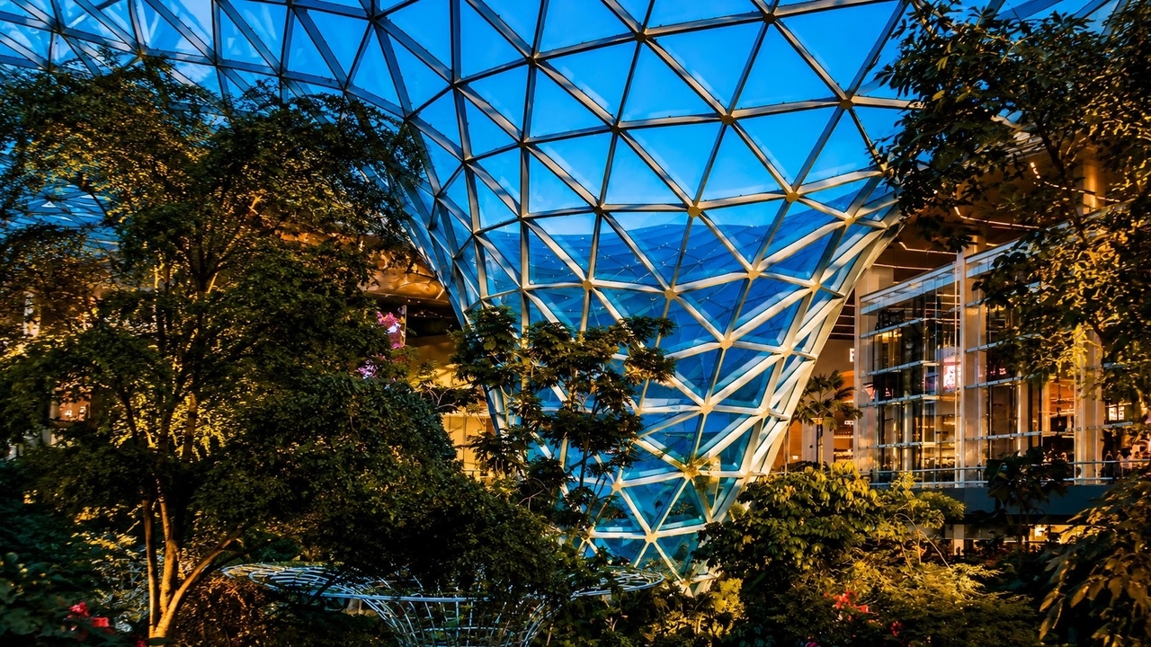 Hamad International Airport's indoor garden dome lit up at dusk with tropical trees and glass architecture 