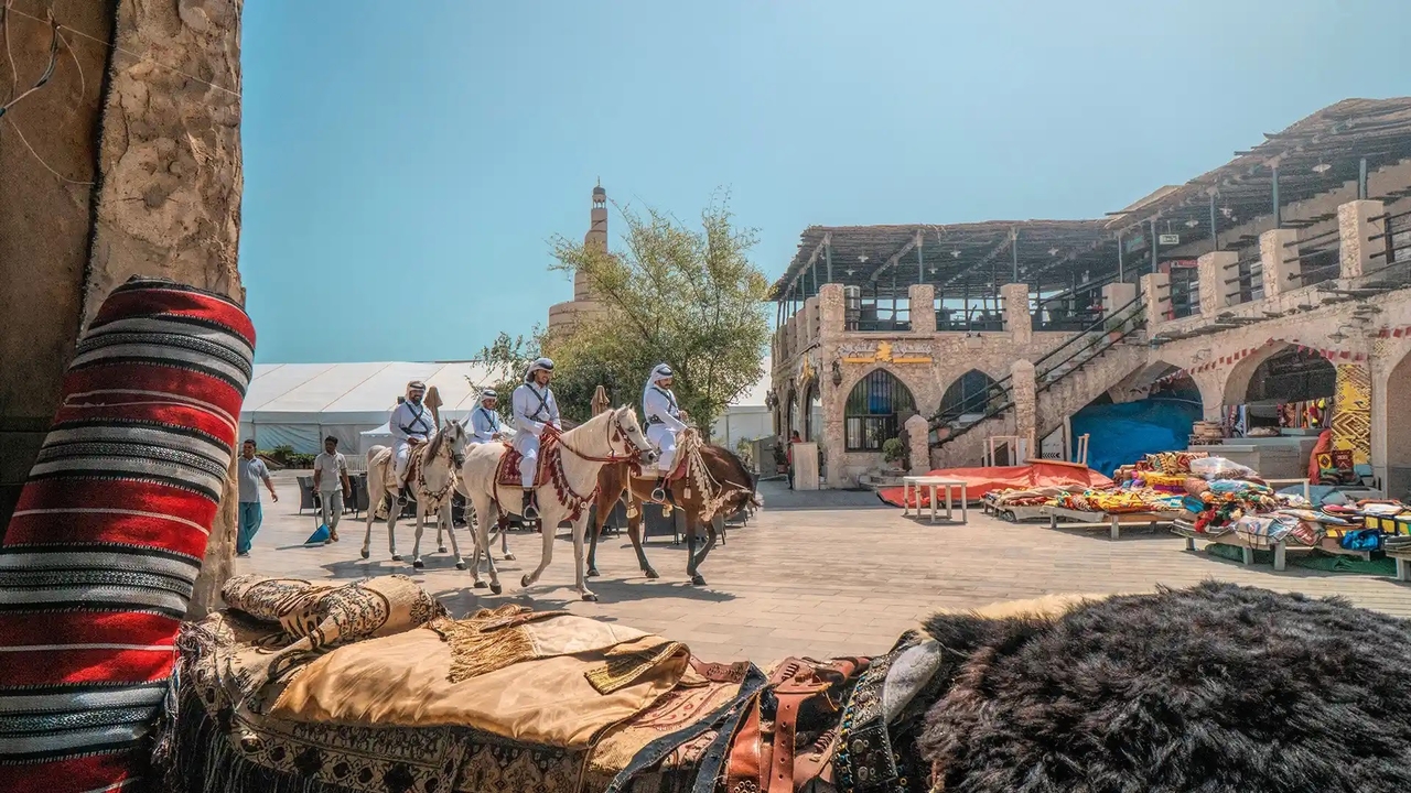 People riding white horses through the traditional stone walkways of Souq Waqif.
