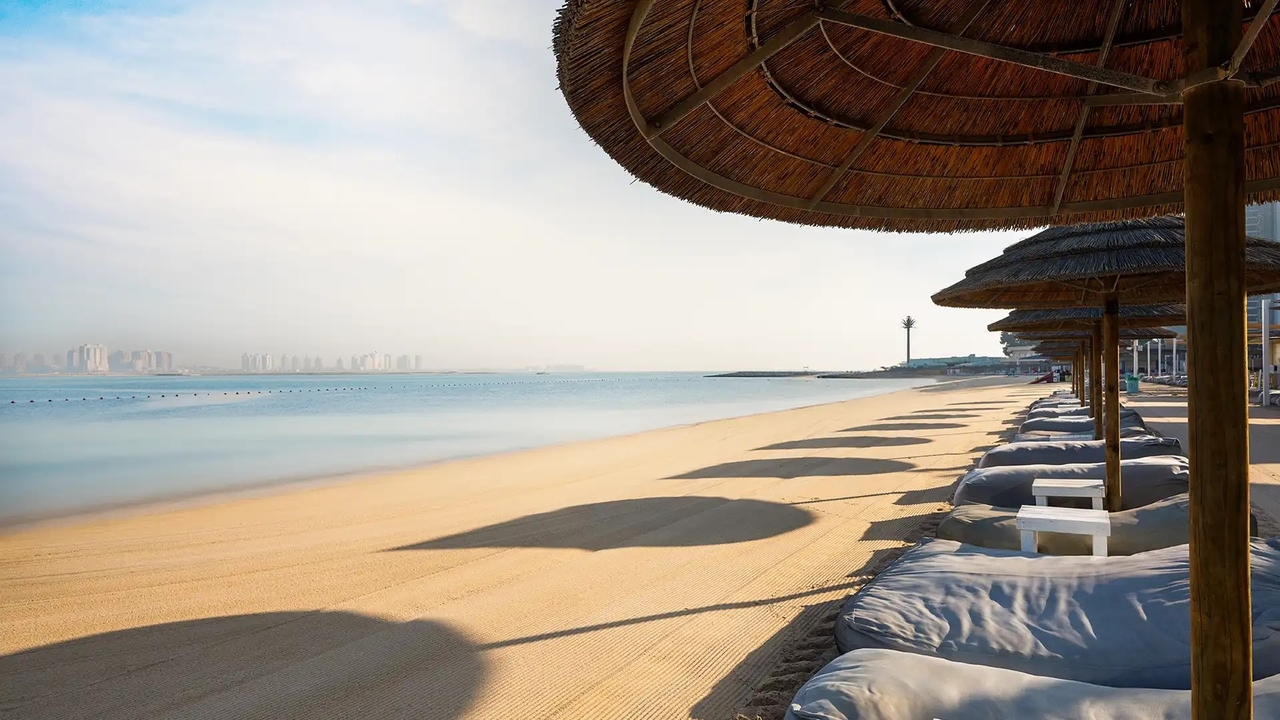 Beach in Doha with thatched umbrellas and loungers