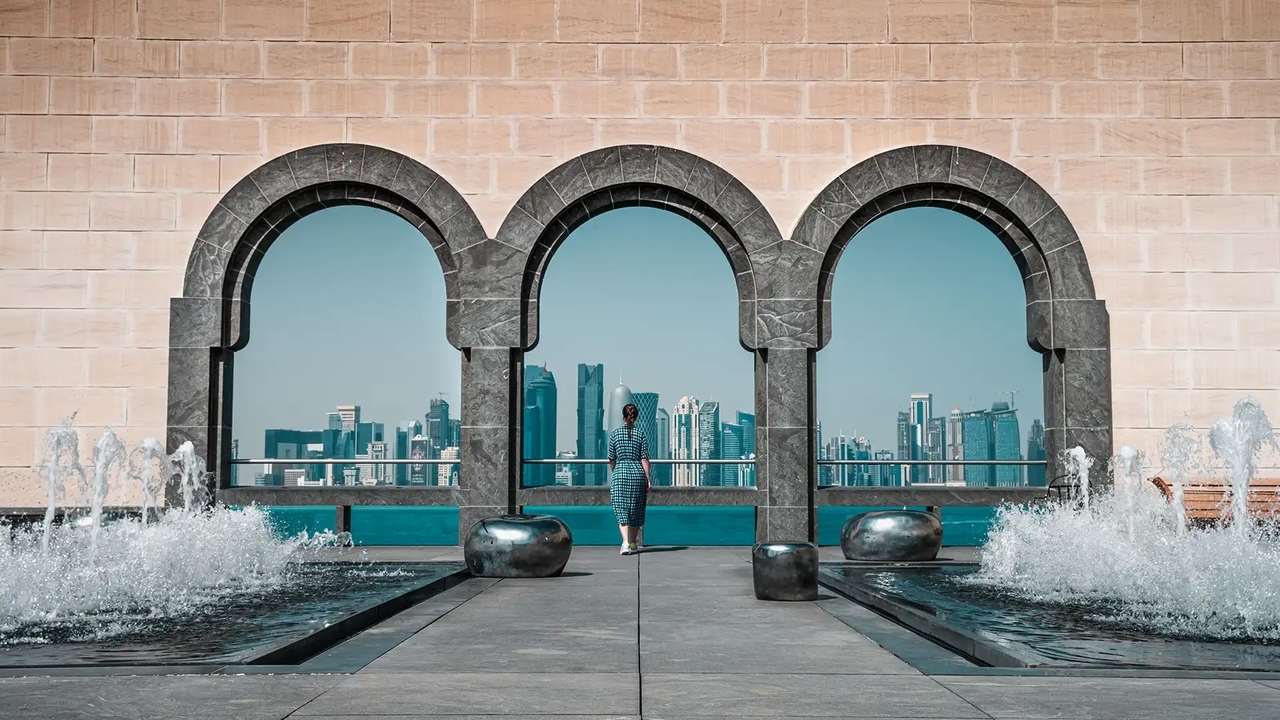 Woman at Museum of Islamic Art arches looking at Doha skyline and fountains.