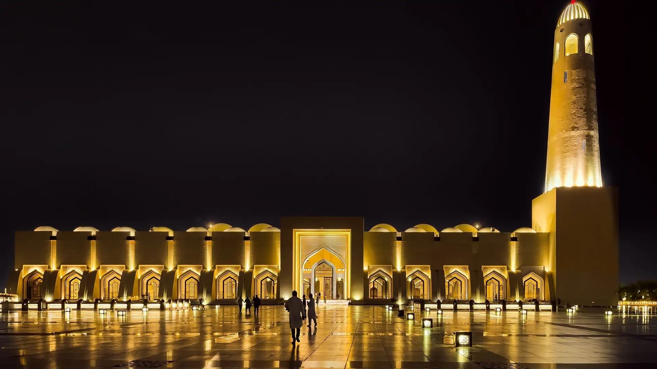 Illuminated minaret and courtyard of the Qatar State Grand Mosque at night
