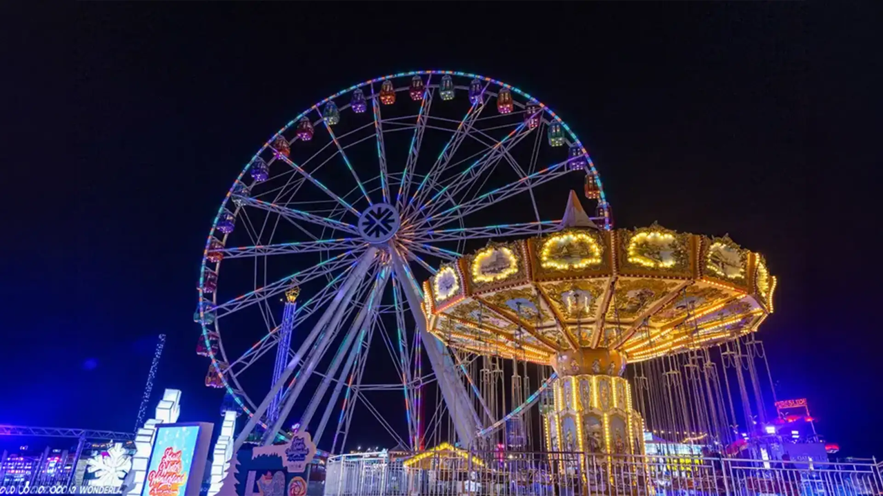 Ferris wheel and swing ride lit up at night at Lusail Winter Wonderland